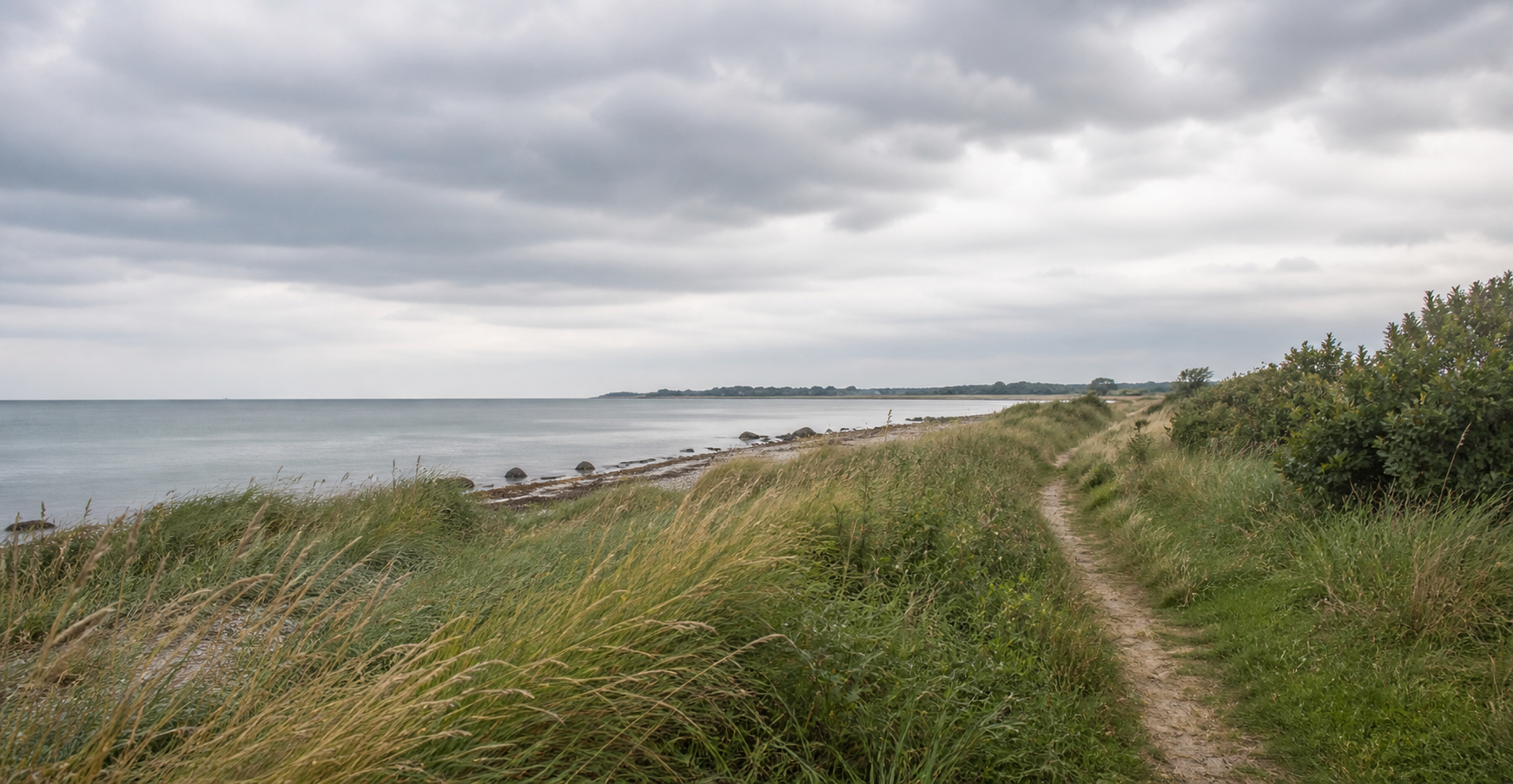 Sti langs Kertemindes rolige kyst under en overskyet himmel